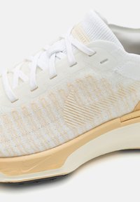 Könnyű fehér sneaker, texturált felső résszel, krém színű részletekkel, fehér fűzőkkel és diszkrét csíkos mintával az oldalán.