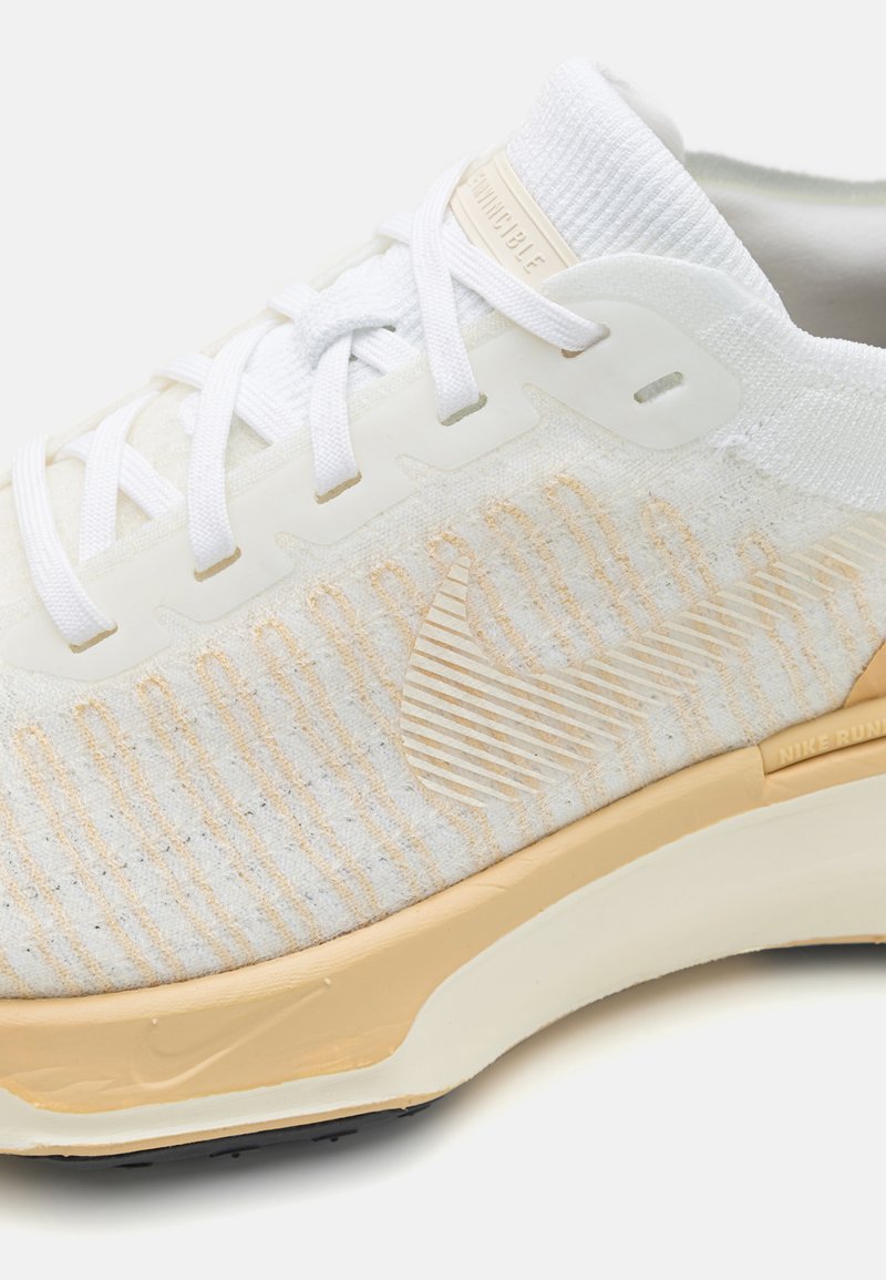 Lichte witte sneaker met een gestructureerde bovenkant en crème accenten, witte veters en een subtiele gestreepte patroon aan de zijkant.