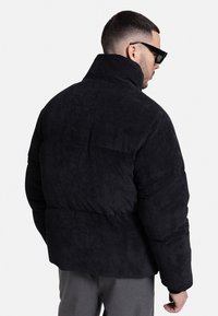 Corduroy puffer jacket in black with a high collar and ribbed texture. Features a relaxed fit and stitched detailing on the back.