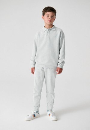 Light grey, long-sleeve polo shirt and matching sweatpants made of soft fabric. Notable details include a small embroidered logo and white sneakers.