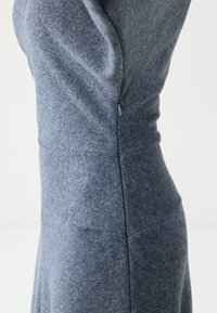 Robe en tissu gris à coupe ajustée, avec des détails de coutures verticales et une fermeture éclair dissimulée sur le côté. Tissu doux et texturé avec une légère élasticité.