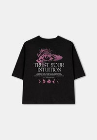 Camiseta de algodón negra con un diseño gráfico que presenta un ojo y el texto "Confía en tu intuición" en rosa, junto con las fases de la luna debajo.