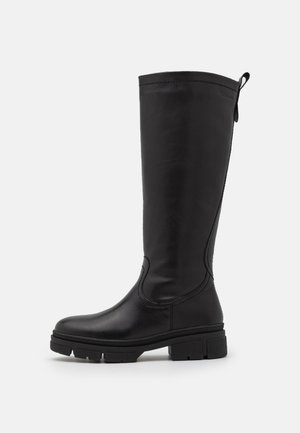 Botte haute en cuir noir avec semelle épaisse, languette de traction à l'arrière et finition lisse, vue de profil sur fond blanc.
