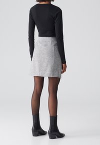 Černý dlouhý rukáv crop top spárovaný se šedou tweedovou sukní s šikmou kapsou, doplněný průhlednými černými punčochami a kotníkovými botami.