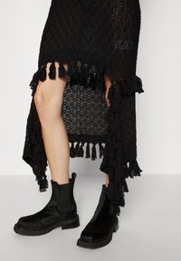 Svart spetskjol med en volangkant och fransar, tillsammans med svarta ankelskor med en texturerad ovandel och en solid gummisula.