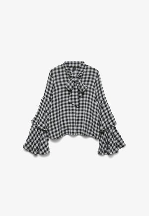 Blouse à carreaux noir et blanc avec manches longues à volants et col noué devant, étalée à plat sur un fond blanc.