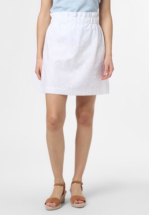 Falda blanca de tela con ojales con cintura elástica, usada con camiseta azul claro y sandalias cuña marrones con punta abierta en una persona de pie.