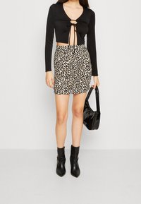 Svart långärmad croppad topp med en knutdetalj vid halslinjen, ihop med en åtsittande leopardmönstrad minikjol och svarta ankelstövlar.