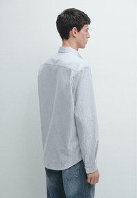 Szara i biała koszula na guziki w paski, z kołnierzem typu kent, długimi rękawami i luźnym krojem, zestawiona z jasnoniebieskimi jeansami.