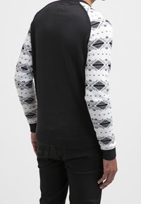 Pull noir avec manches blanches à motifs géométriques, doté d'un ourlet et de poignets côtelés ; vue de dos montrant le détail des manches et la forme générale.