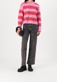 Vaaleanpunainen ja punainen raidallinen pörröinen neule yhdistettynä harmaisiin tähtikuvioisiin leveälahkeisiin farkkuihin ja paksupohjaisiin mustiin saappaisiin. Pitää mustaa laukkua kädessään.