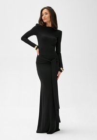 Długa czarna sukienka z elastycznej tkaniny, z dopasowaną górą, długimi rękawami i węzłem w talii, z szeroką spódnicą.
