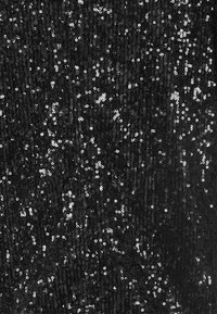 Czarna tkanina pokryta odblaskowymi srebnymi cekinami, tworząc teksturową powierzchnię o zróżnicowanych odbiciach światła i rozproszonych wzorach.