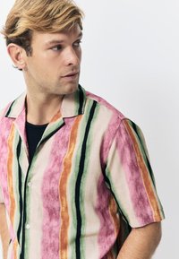 Chemise à manches courtes en tissu léger avec des rayures verticales roses, vertes, orange et noires, dotée d'un col style camp et d'une fermeture à boutons.