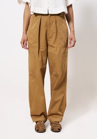 Tan cargobroek van katoen, met een wijdere snit, plooien bij de taille en twee voorzakken voor gebruiksgemak. Gecombineerd met bruine sandalen.
