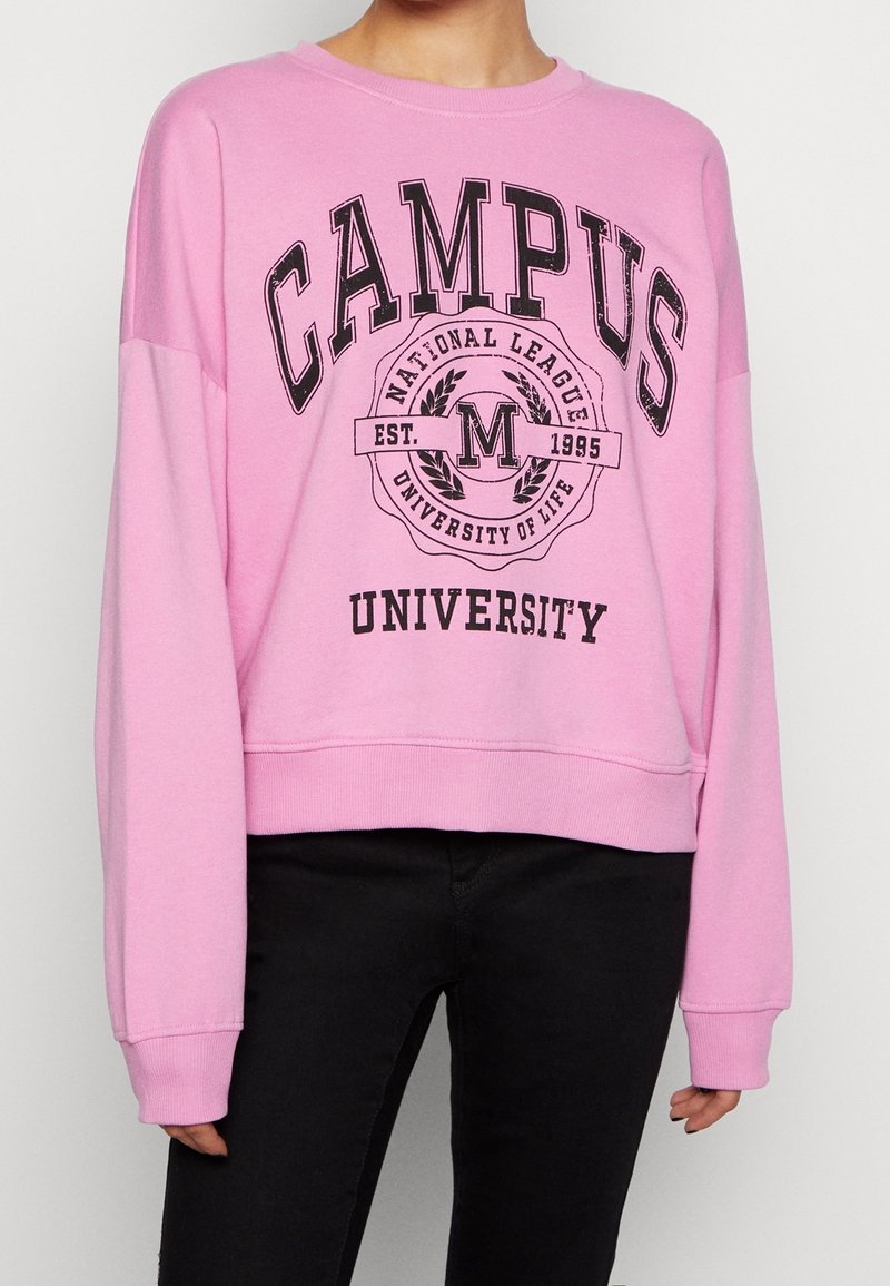 Sudadera de algodón rosa con escote redondo, hombros caídos y un logo impreso de "CAMPUS UNIVERSITY" en negro en la parte frontal.