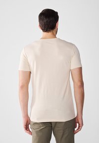 Beige kortermet t-skjorte laget av mykt stoff, med rund halsutskjæring og vanlig passform, samt en lett, glatt tekstur.
