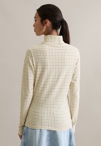 Koszula z długim rękawem, lekka, z wysokim kołnierzem, wykonana z kremowej tkaniny w żółtą kratę. Gładka faktura; dopasowany fason.