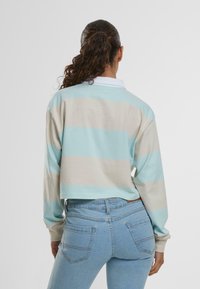 Un sweat-shirt raccourci avec des rayures horizontales bleu clair et beige, des manches longues et un col blanc. Associé à un jean bleu clair ajusté.