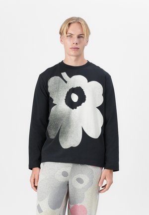 Chemise noire à manches longues avec un grand motif graphique de fleur blanche. Le tissu est lisse avec une coupe décontractée. Pantalons à motifs gris complémentaires.