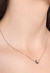 Srebrny naszyjnik z delikatnym łańcuszkiem, który prezentuje wzór w kształcie sierpa księżyca oraz mały przezroczysty kamień jako akcent. Gładka tekstura, minimalistyczny styl.