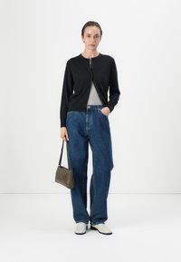 Cardigan nero a bottoni sopra una maglietta grigia, abbinato a jeans blu larghi. Una piccola borsa grigia con texture e scarpe chiare.