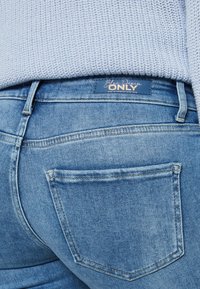 Blå jeans med lys vask, med en baklomme og en etikett som sier "Blue Denim ONLY" ved linningen.