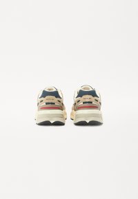 Sport sneakers met een bovenwerk in tan en marineblauw, voorzien van suède en mesh elementen, rode accenten en een zware witte zool.