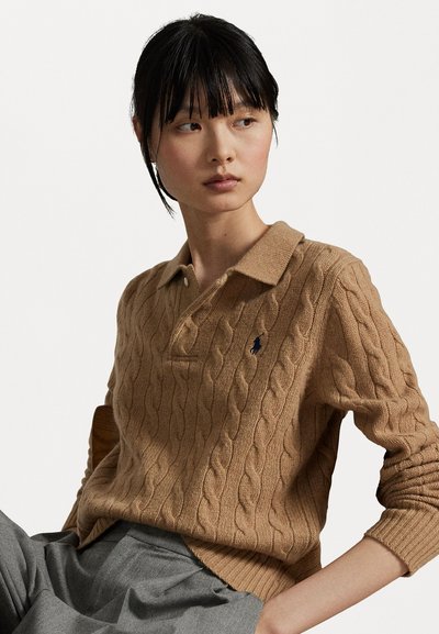 Cable-knit beige polo sweater with long sleeves, a folded collar, and a small blue logo on the left chest. Soft texture and relaxed fit.