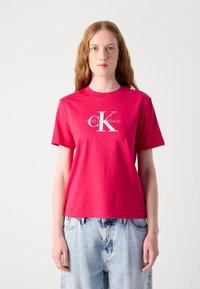 Camiseta de algodón de color rosa brillante con mangas cortas y cuello redondo, que presenta un diseño de logo blanco en el centro. Ajuste casual.
