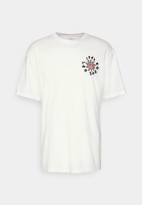 Camisa de algodón blanca con mangas cortas, que presenta un diseño gráfico circular multicolor en el pecho que incluye texto y un símbolo de paz.