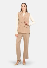 Beige dvojřadý vest do V s ostrými klopami, kombinovaný s odpovídajícími slim kalhotami. Hladká tkanina, minimalistický design a výrazné knoflíky.