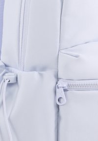 Svijetloplavi teksturirani ruksak od tkanine, s bijelim detaljima od hardvera, zatvaračem i vezicom sa strane.