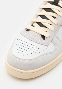 Sneaker con tomaia in suede grigia e pannello in pelle bianca, caratterizzato da dettagli perforati, lacci crema e suola in gomma beige.