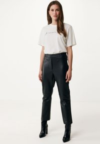 Sorte faux læderbukser med en glat tekstur, tætsiddende design og høj talje, parret med en løs hvid t-shirt med kursiv skrift.