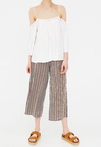 White off-the-shoulder top with a scalloped trim, paired with striped cropped pants in various colors. Brown platform sandals complete the look.