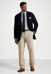 Tamsiai mėlynas švarkas, šviesiai mėlyna languota marškiniai, tamsi kaklaraištis, smėlio spalvos chinos kelnės, rudi odiniai bateliai. Balta kišenėlė ir tekstūruota kaklaraiščio detalė.