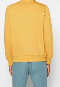Sudadera amarilla de cuello redondo hecha de una tela suave, con un cuello y puños acanalados, de corte holgado y textura lisa.