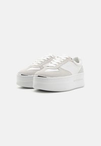 Hvite plattform-sneakers med grå semsket tilbehør, rund tå, snøring, og sølvmetallisk detaljer foran. Teksturerte gummisåler.