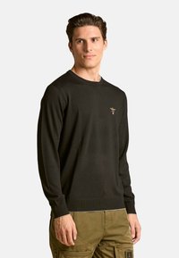 Maglione nero a maniche lunghe con scollo rotondo, con un piccolo logo ricamato sul petto. Realizzato in un tessuto morbido e strutturato.