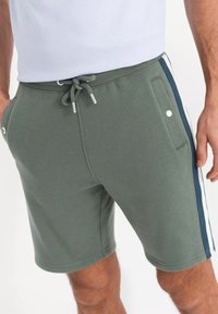 Shorts en mélange de coton verts avec une taille élastique à cordon, des poches latérales et des rayures verticales bleu marine et blanches sur les côtés.