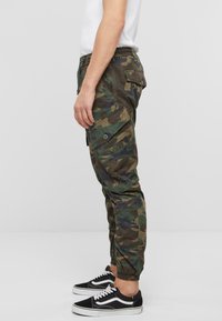 Pantalones cargo de camuflaje en tonos variados de verde y marrón, con bolsillos laterales, puños elásticos y un corte relajado.