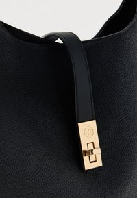 Svarthåndveske i skinn med en teksturert overflate, utstyrt med en lås i gullfarge og et glatt, flatt håndtak festet på toppen.