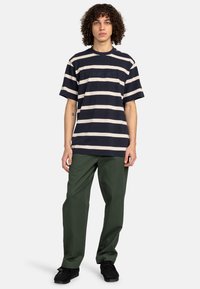Marineblå og creme-stribet bomulds t-shirt med korte ærmer og broderet logo på fronten, parret med grønne bukser og sorte sko.