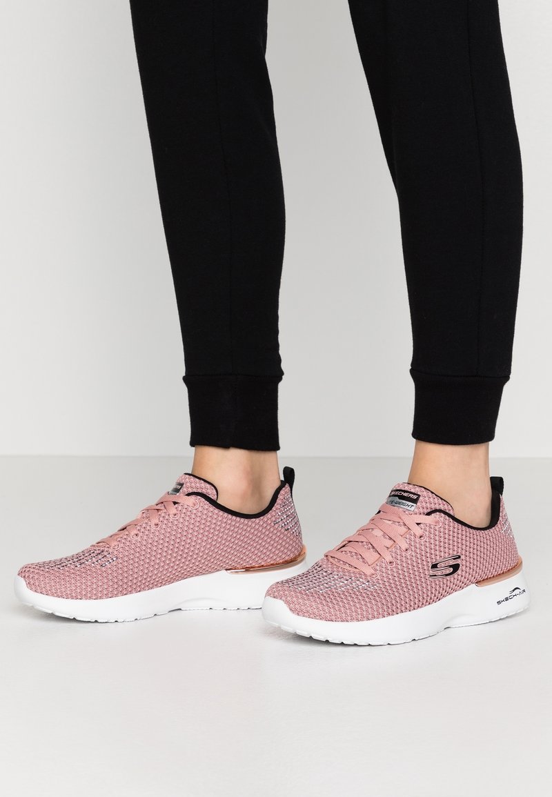 Ljusrosa mesh-sneakers med vita sulor, som har en roséguld-accent, svart kant och snörning, designade för komfort och andningsförmåga.
