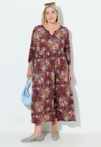 Vestido floral en burdeos oscuro con mangas de tres cuartos, escote en V y cintura fruncida. Un bolso azul y unas bailarinas grises completan el conjunto.