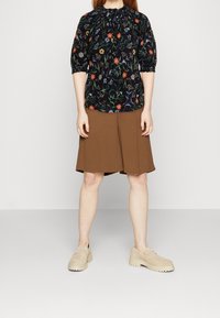 Blommig blus i mörk tyg med puffärmar, kombinerad med en brun plisserad kjol. Ljusmockaskor utan snörning med tjocka sulor.