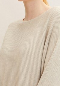 Beige gerippter Pullover mit lockerer Passform, ausgestattet mit einem weiten Halsausschnitt und strukturierten Details in vertikalen Mustern. Weiches, leichtes Material.