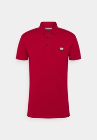 Polo rouge en coton avec un col, une patte de boutonnage à trois boutons, des manches courtes et un petit écusson noir sur la poitrine gauche.