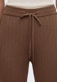 Gros plan sur un pantalon en maille côtelée marron avec un cordon noué à la taille, porté avec un haut côtelé crème.